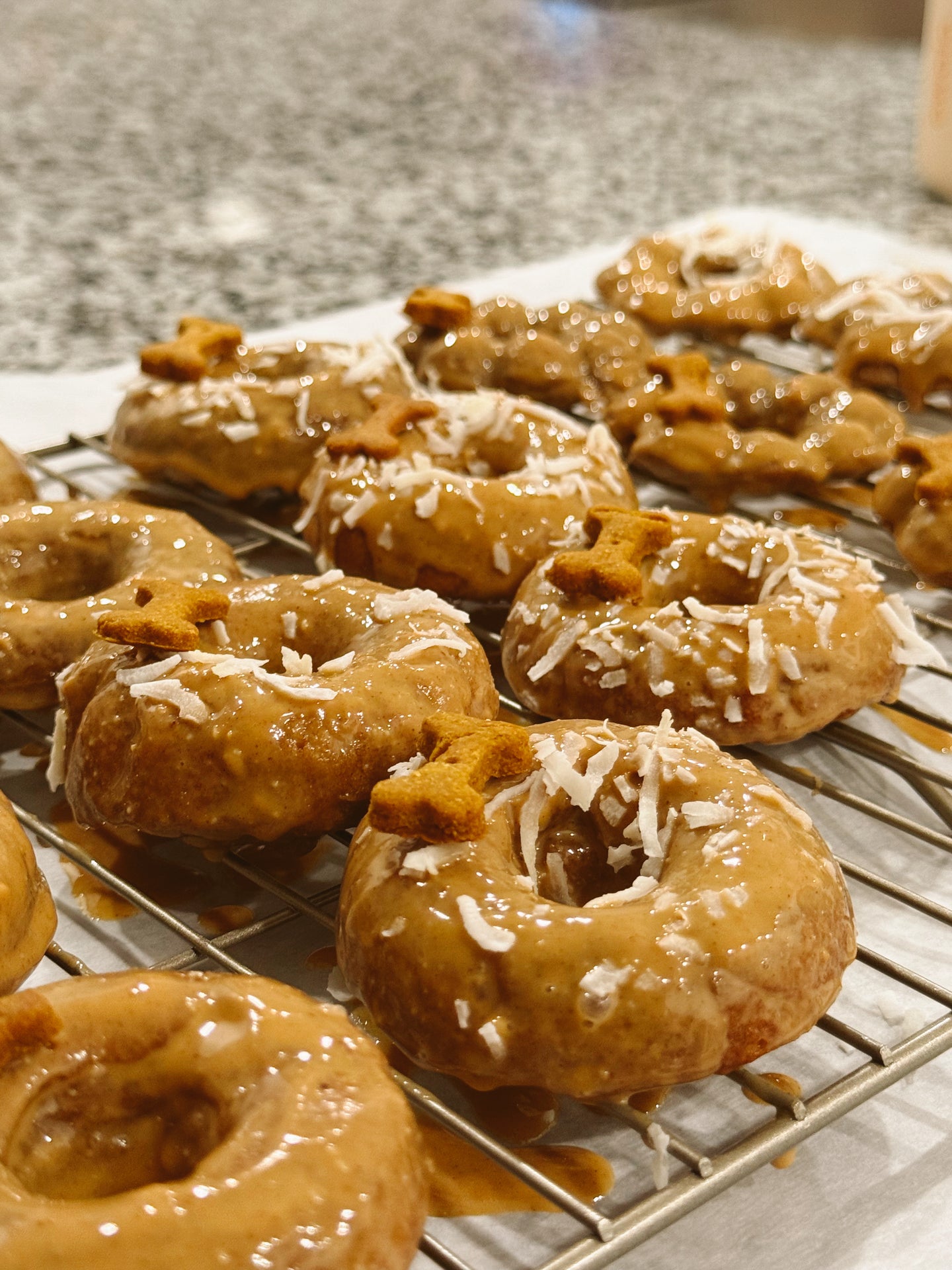 Donuts with glaze and coconut shavings on a cooling rack.